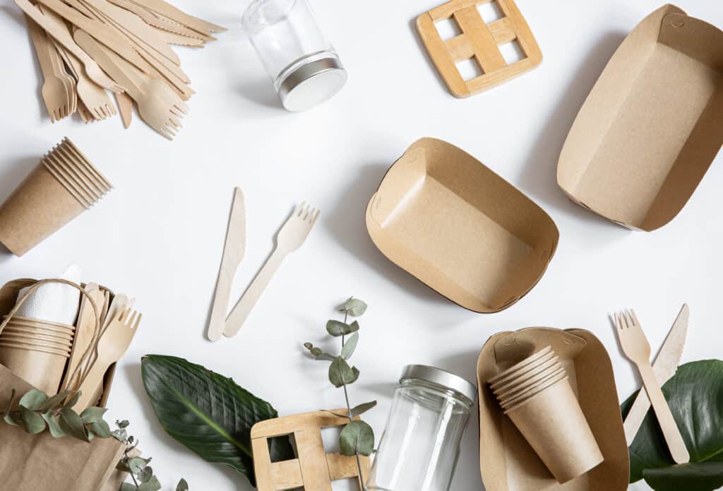 Composition with disposable paper and reusable tableware with natural leaves top view.